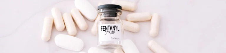 Fentanyl pills and a syringe surrounding a fentanyl bottle