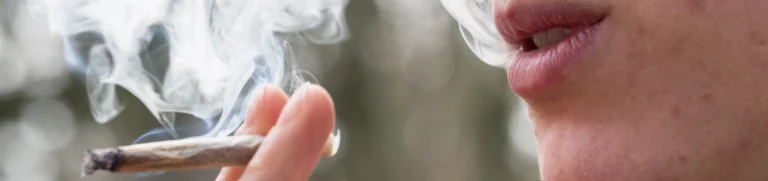 Person holds a marijuana cigarette near their face and exhales