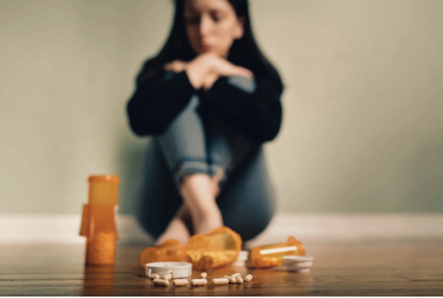 Depressed woman sits near a pile of spilled opiate pills