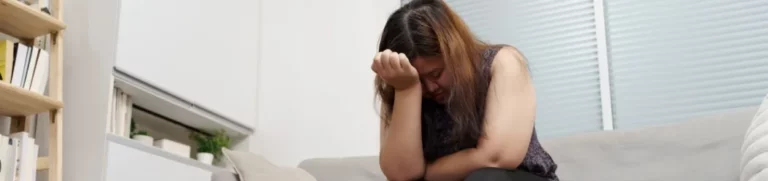 Depressed woman sits on a couch with her head in her hand