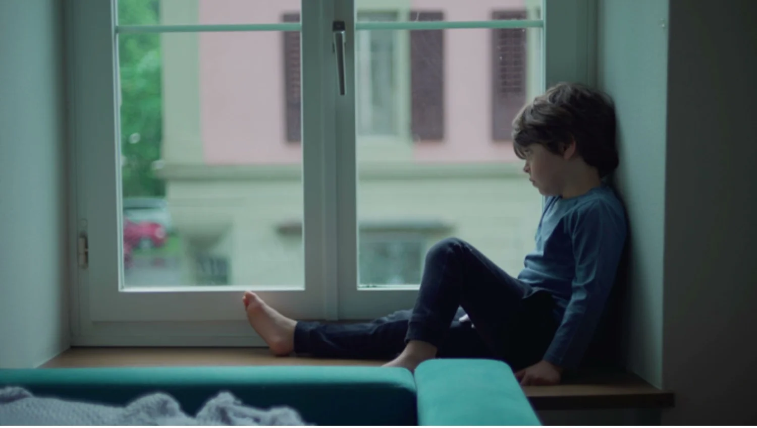 Sad young boy sits in a windowsill and looks out the window