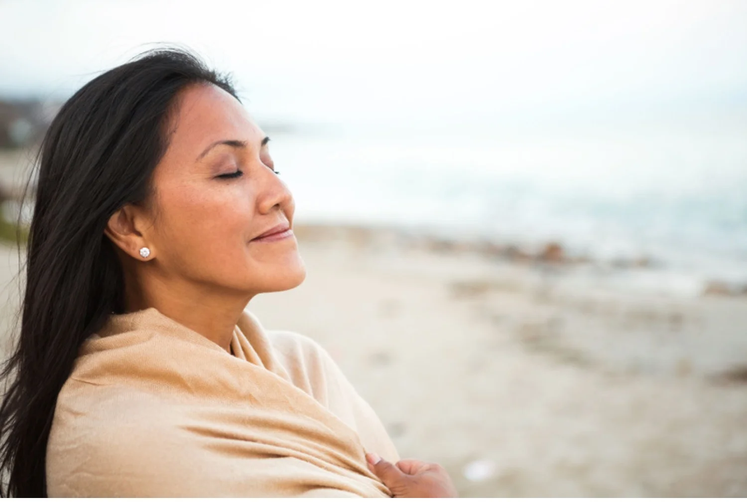 Woman on beach smiles contentedly with eyes closed