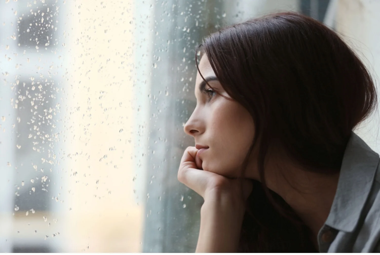 Young depressed woman looks out the window on a rainy day