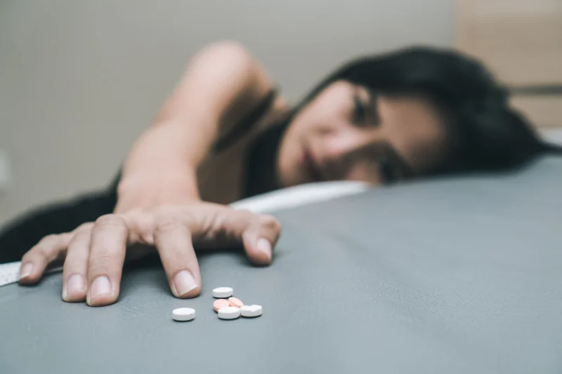 Young sad looking woman reaches for a pile of pills