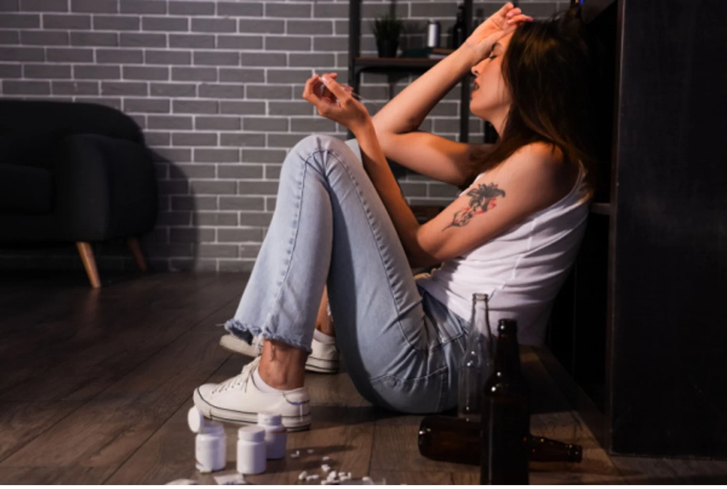 Young woman with BPD who is addicted to pills and alcohol sits on the floor looking distressed