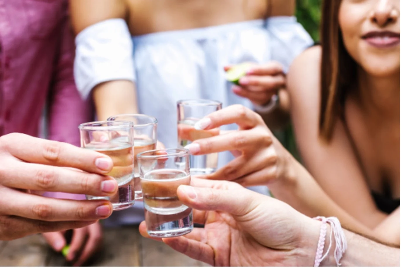 Group of young women clink shot glasses together