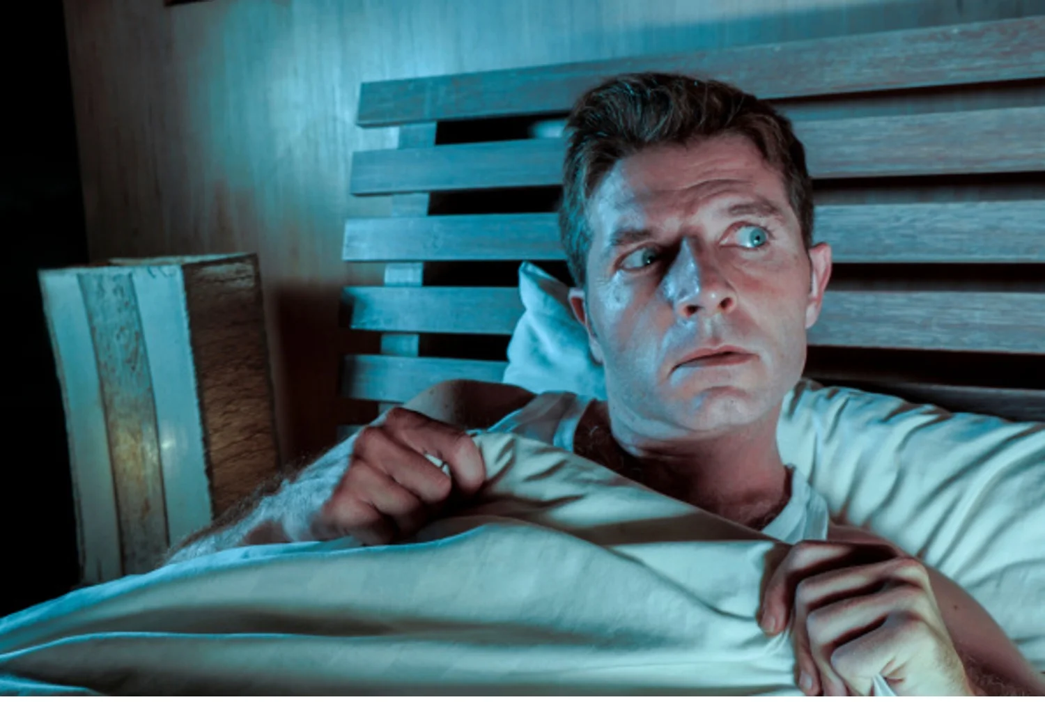 Paranoid man sits awake in bed looking suspiciously around