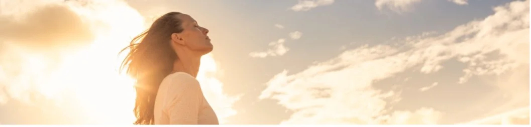 Woman looks up with eyes closed with radiant sky behind her