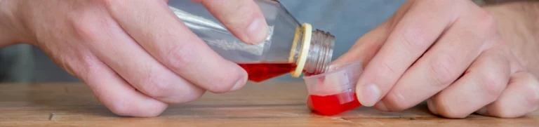 Hands pouring a dose of dextromethorphan into a small plastic cup