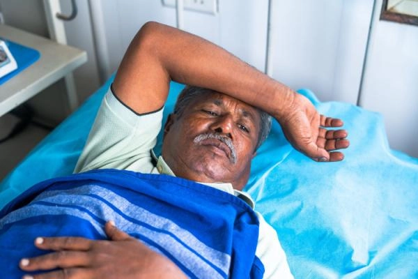 Older man going through alcohol detox lays in hospital bed looking fatigued