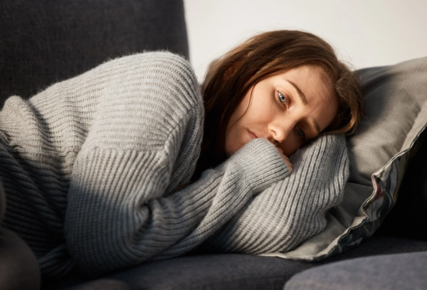 Woman going through tramadol withdrawal lays on couch with pained expression