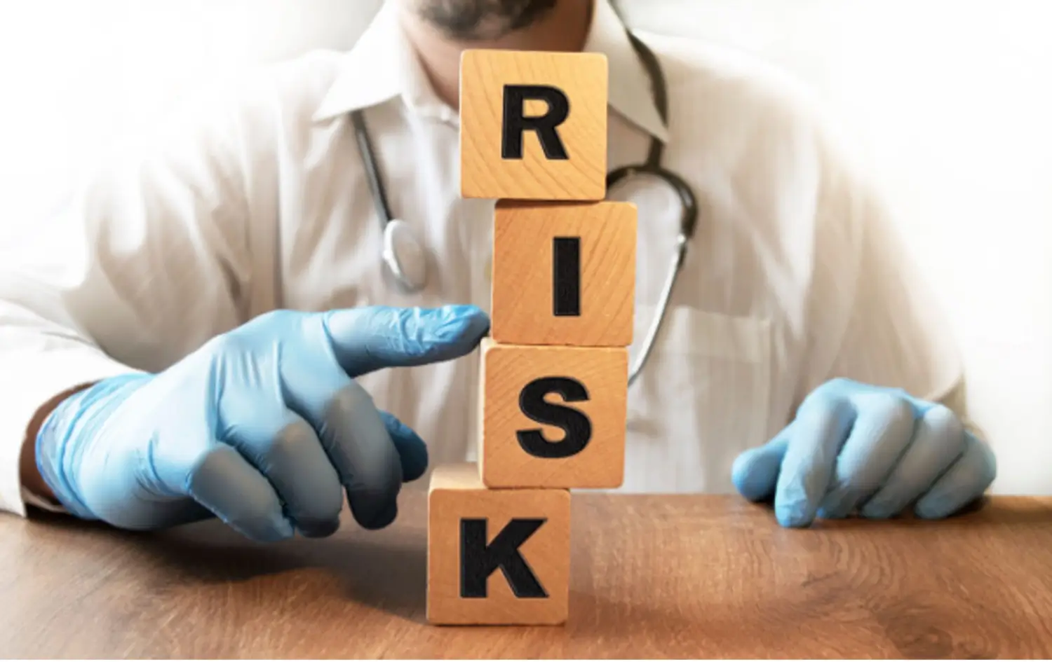 Doctor pushes over stack of blocks that spell out the word “RISK”