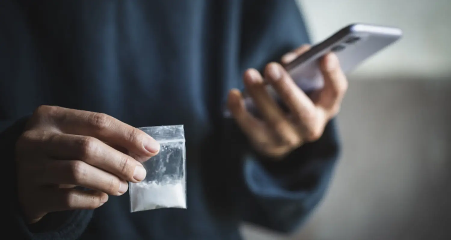 Drug dealer holds bag of drugs in one hand and phone in the other
