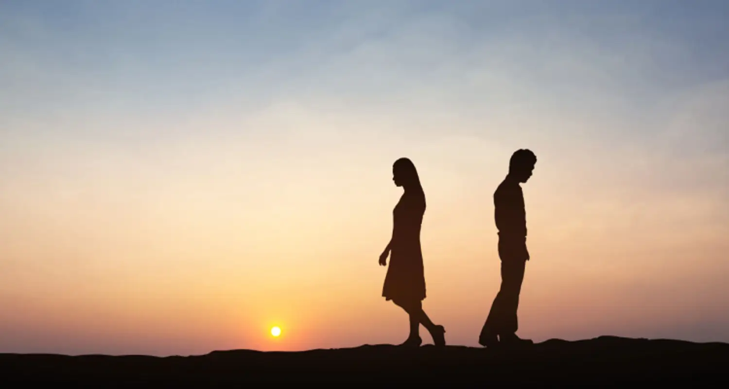 Silhouettes of a man and a woman walking away from each other with sun setting in the background