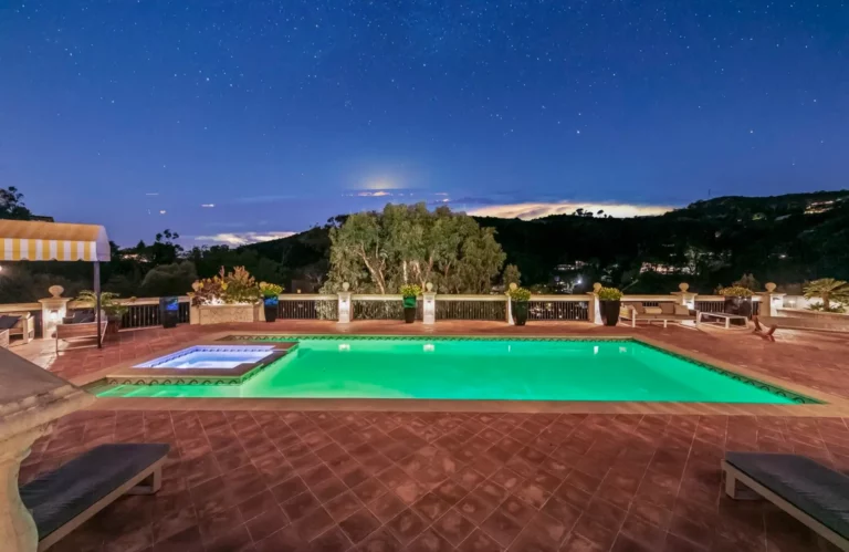 Luxurious outdoor pool lit up at night against the silhouette of surrounding mountains