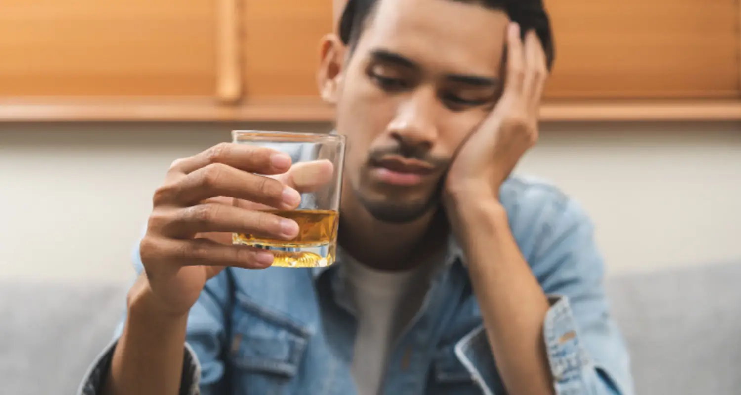 Drunk and sad-looking man holds glass of whiskey