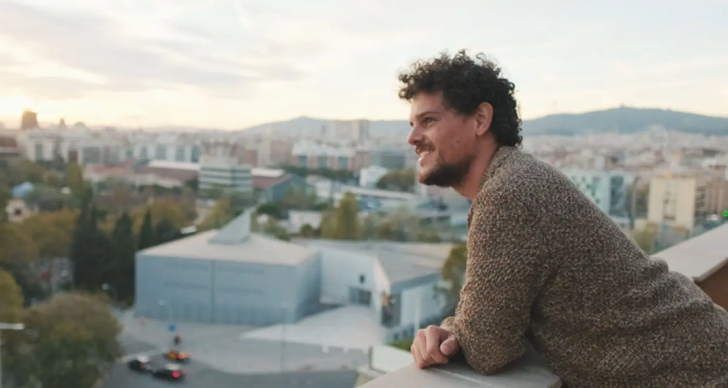 Happy, confident man leans on balcony railing overlooking city below