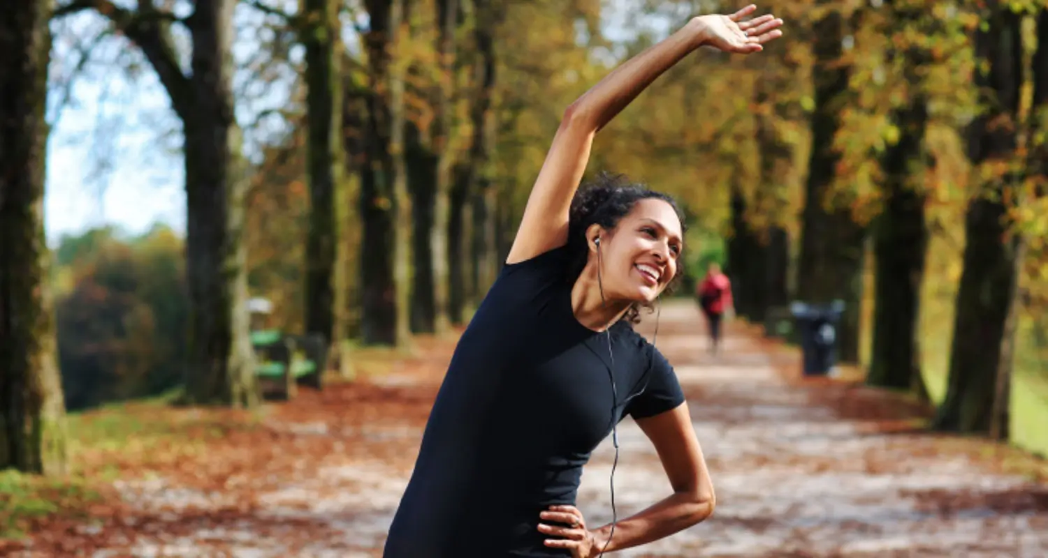 Happy woman does stretches while on a jog on a tree-lined walkway