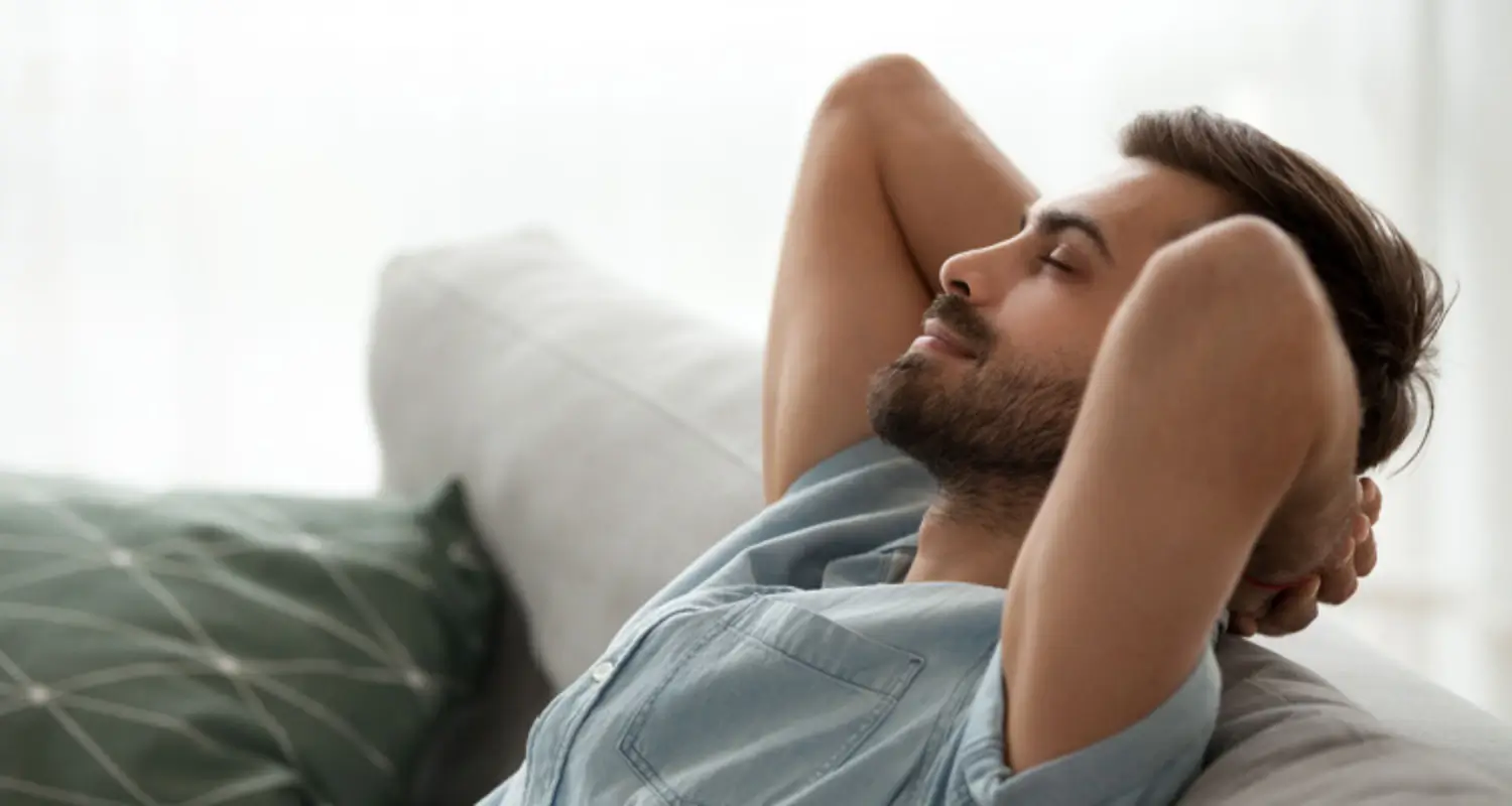 Relaxed, happy looking man reclines head back on the couch