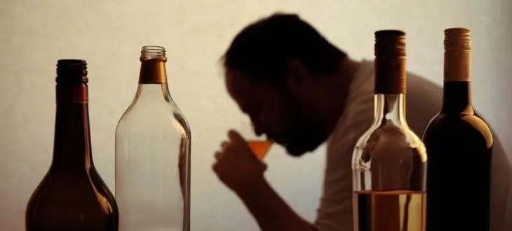 Silhouette of man drinking alcohol with bottles of beer and wine in the foreground