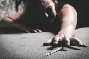 Person struggling with heroin addiction reaching toward a syringe, highlighting the need for professional heroin rehab and treatment