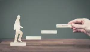 erson silhouette stepping upward while a hand adds a “Recovery” block, representing addiction recovery and staying sober.