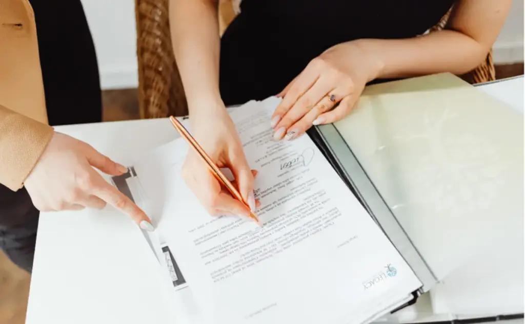 Hands signing admission paperwork with guidance, representing assistance with travel documents for addiction treatment.